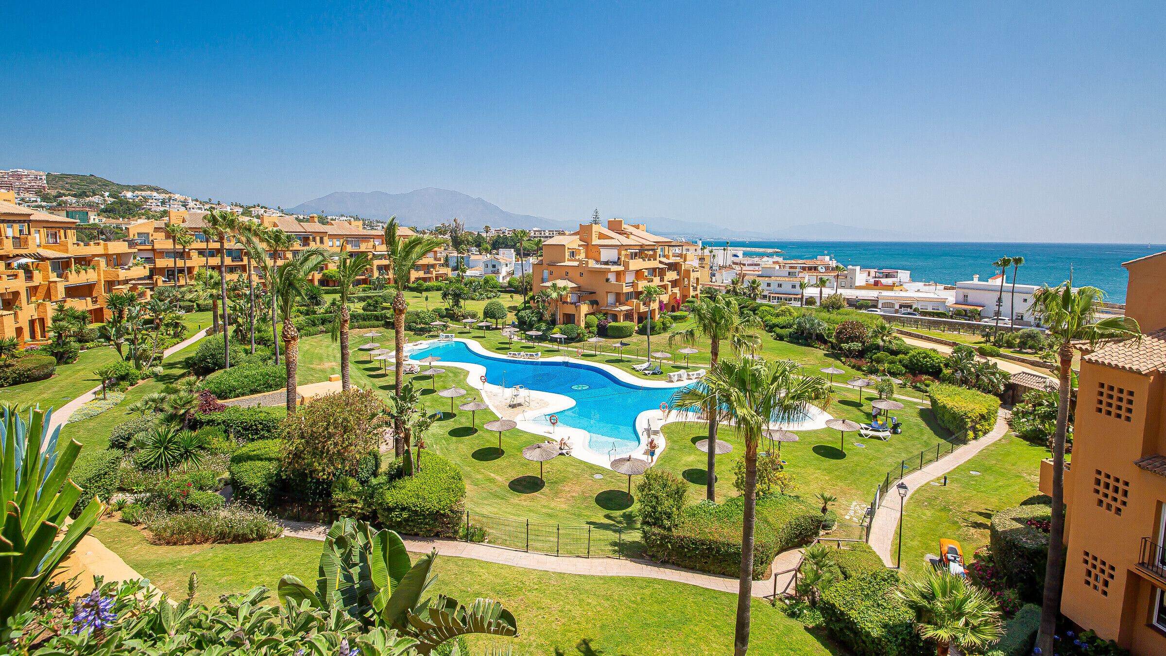 Un resort con piscina central, exuberante vegetación y vista al mar.