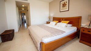 A bedroom with a wooden bed, white bedding, a small bedside table, a lamp, and a framed picture on the wall.