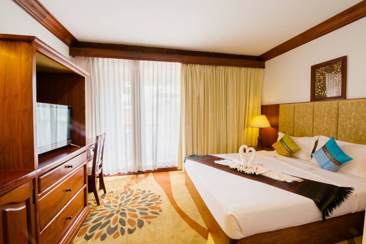 Una habitación de hotel con una cama, un escritorio con televisión, una lámpara y una ventana con cortinas.