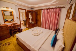 A hotel room with a bed, a wooden desk, a chair, a mirror, and a wardrobe.