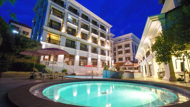 Un hotel con piscina, mobiliario exterior y fachada bien iluminada.