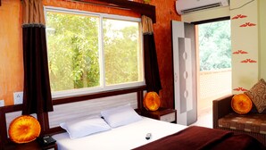Habitación de hotel con una cama grande, una mesita de noche con teléfono, una ventana con cortinas y vistas a zonas verdes.