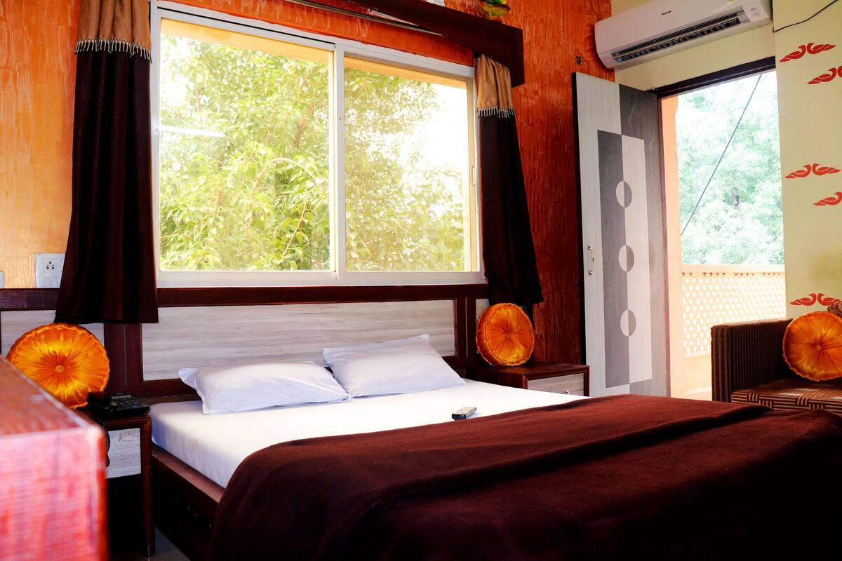 Ein Hotelzimmer mit großem Fenster, einem Bett mit weißen Laken und einer braunen Decke.