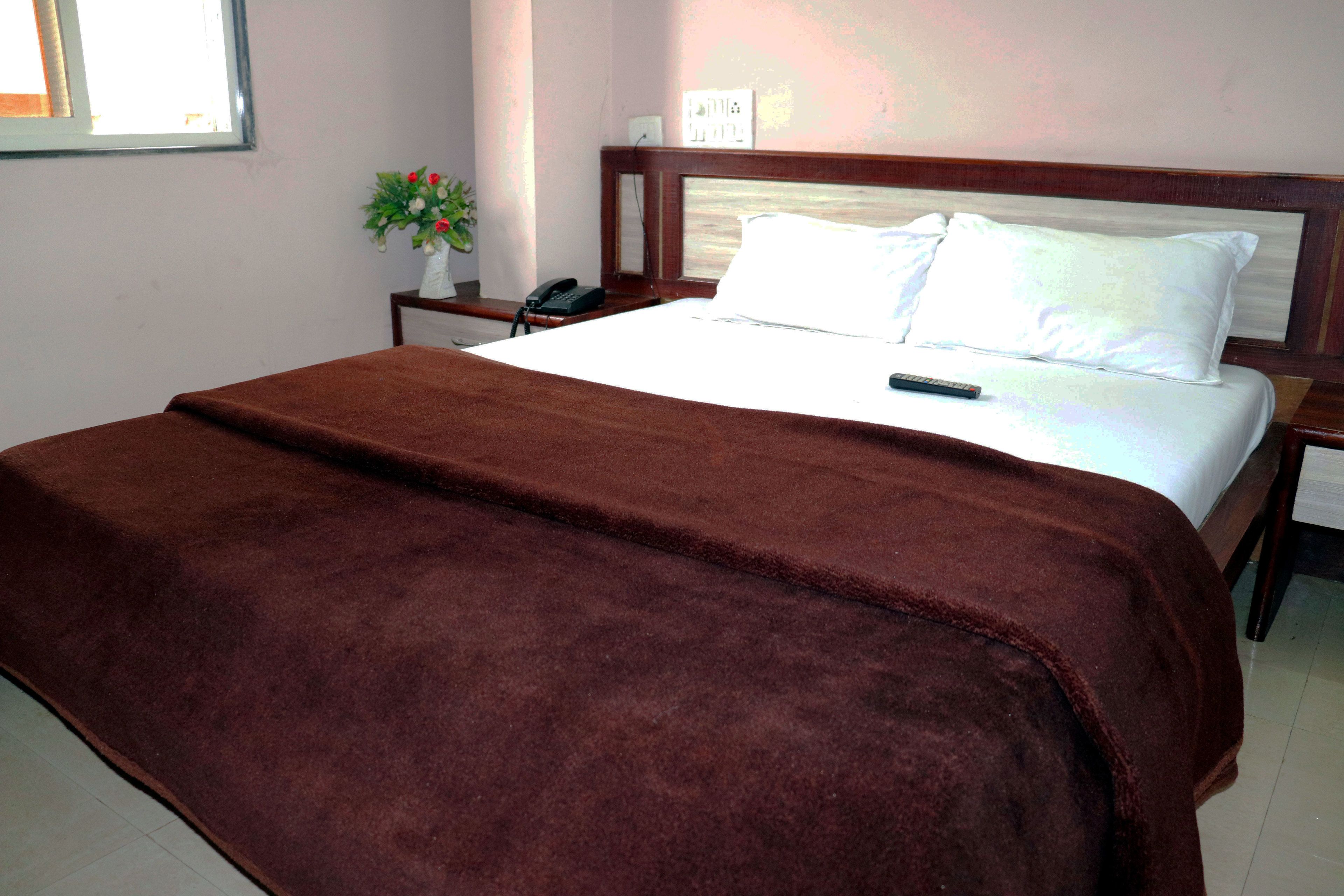 A neatly made bed with a brown blanket, a bedside table with a phone, and a wall-mounted light fixture.