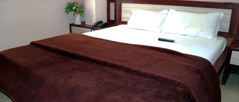 A neatly made bed with a brown blanket, a bedside table with a phone, and a wall-mounted light fixture.