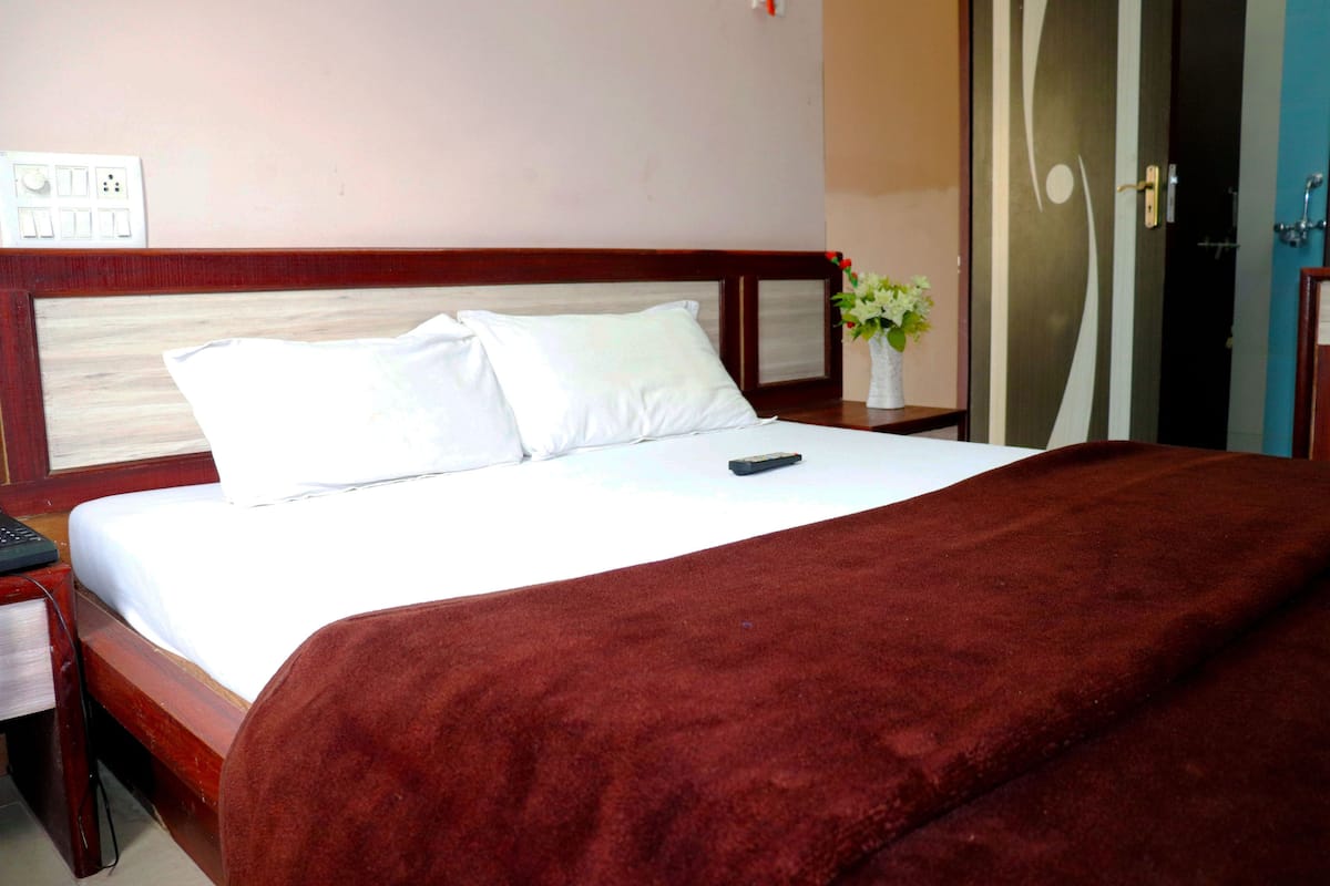 Ein Hotelzimmer mit einem Bett, einem Nachttisch, einer Fernbedienung, einer Vase mit Blumen und einer Tür.