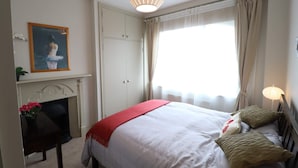 Une chambre à coucher avec un lit, une cheminée, une fenêtre avec des rideaux et un tableau au mur.