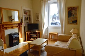 Un salon avec une cheminée, un téléviseur, un canapé et une fenêtre donnant sur des immeubles.