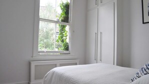 Een slaapkamer met een groot raam, witte muren en een radiator.