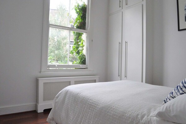 A bedroom with a large window, white walls, and a radiator.