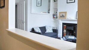 Een woonkamer met een donkere bank, een open haard en een boekenkast.