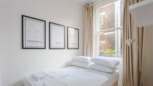 A neatly made bed with white linens and pillows, a framed map of Farringdon, Texas, and a framed map of Lowestoft. - Stylish Apartment in Central London - Farringdon (London)