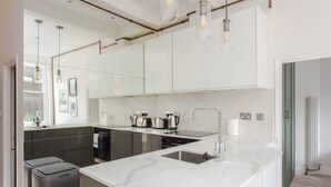 A modern kitchen with white marble countertops, stainless steel appliances, and pendant lighting. - Stylish Apartment in Central London - Farringdon (London)