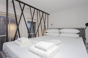 A neatly made bed with white linens and pillows, a modern black metal headboard, and a window with frosted glass. - Stylish Apartment in Central London - Farringdon (London)