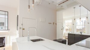 A modern kitchen with a large island, white cabinetry, and pendant lighting. - Stylish Apartment in Central London - Farringdon (London)