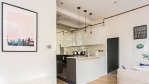 A modern kitchen with a central island, pendant lights, and a view into the dining area. - Stylish Apartment in Central London - Farringdon (London)