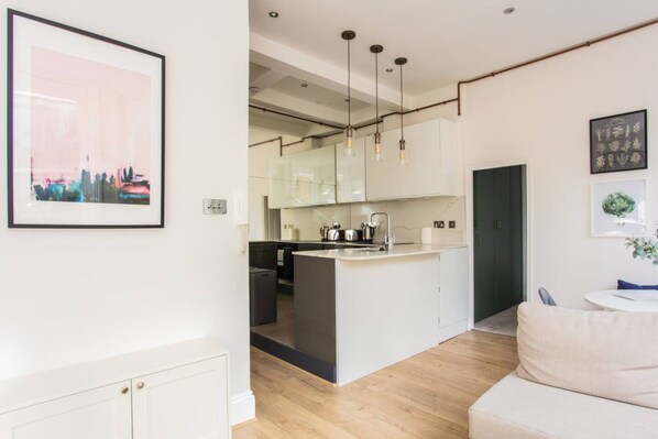A modern kitchen with a central island, pendant lights, and a view into the dining area. - Stylish Apartment in Central London - Farringdon (London)