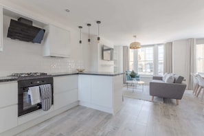 A modern kitchen with white cabinetry, a central island, and a dining area with a sofa and table. - Stunning 3 Bedroom 2 Bath in Fantastic Location (London)