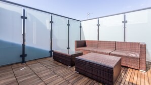 Een terras op het dak met rieten meubilair, glazen wanden en een houten terras.