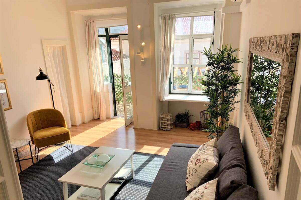 A living room with a sofa, a coffee table, a floor lamp, and a large window with curtains.