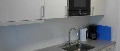 A compact kitchen with white cabinets, a microwave, a sink, and a coffee maker.