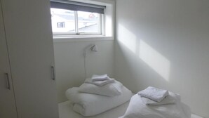 A small, clean room with a bed, a window, and a towel rack. - IceCap Apartments (Ilulissat)