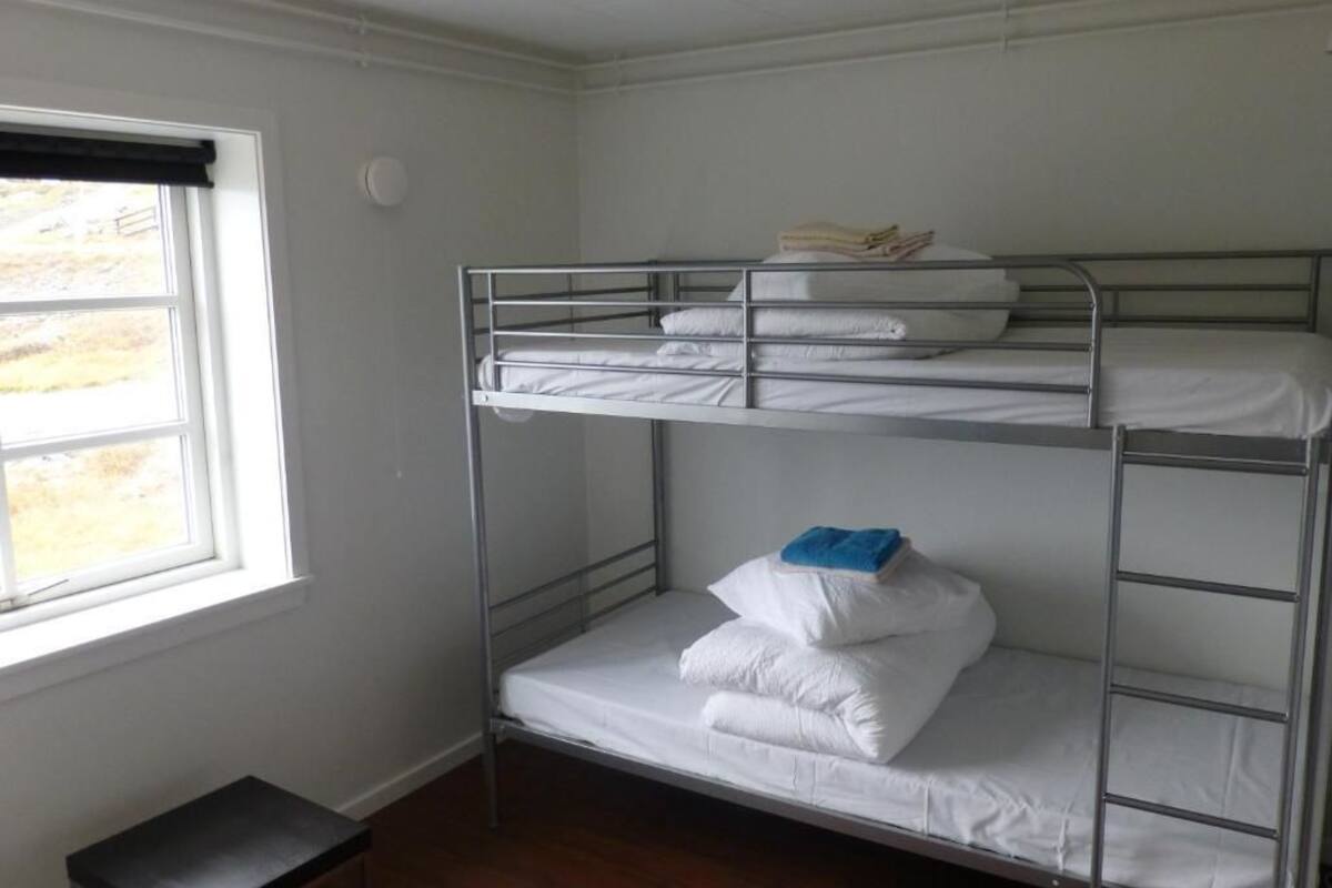 A bunk bed room with a window, a small table, and a door.