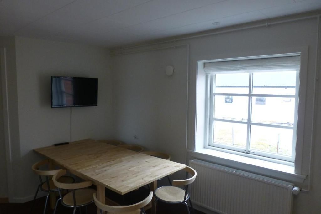 A room with a wooden table, four chairs, a flat-screen TV mounted on the wall, and a window with a view of the outside.