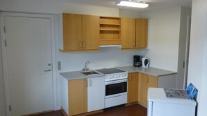 A compact kitchen with white cabinets, a stove, and a coffee maker. - IceCap Apartments (Ilulissat)