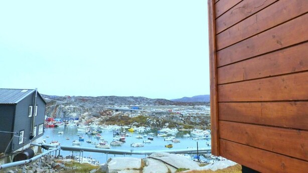 A harbor with boats, a building, and rocky terrain in the background. - IceCap Apartments (Ilulissat)