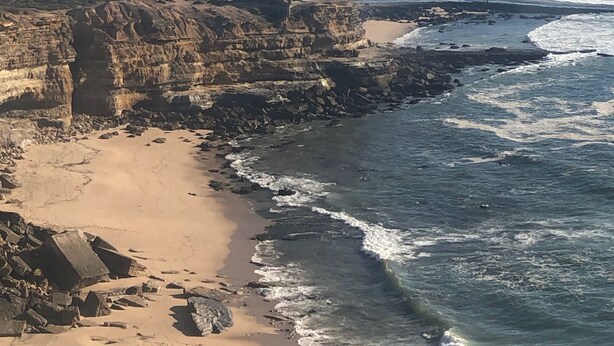 A coastal landscape with rocky cliffs, a sandy beach, and the ocean.
