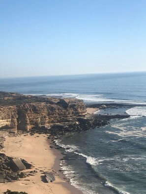 A coastal landscape with rocky cliffs, a sandy beach, and the ocean.