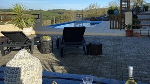 A poolside setting with a table, a bottle of wine, a glass, and a plate with food.