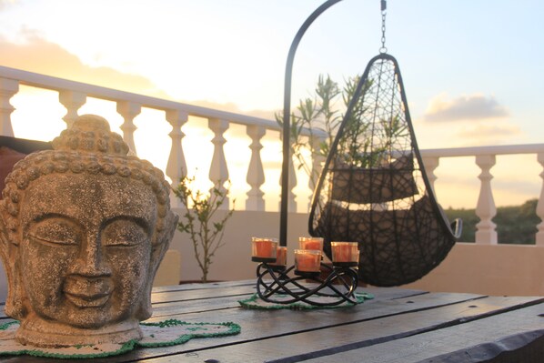 A Buddha head sculpture, a hanging chair, and candles on a balcony.