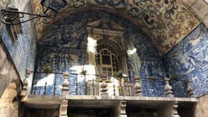 An ornate room with intricate blue and gold tile work on the walls and ceiling, a balcony with balustrades, and a large arched window.