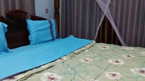 A bed with a blue bedspread and floral-patterned blanket, a wooden headboard, and a mosquito net. - Faida Hill Motel (Kampala)