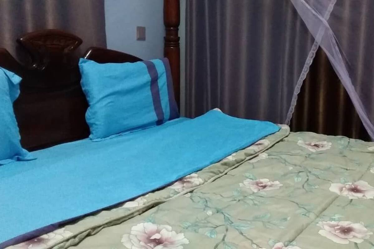 Una cama con colcha azul y manta estampada con motivos florales, cabecera de madera y mosquitero.