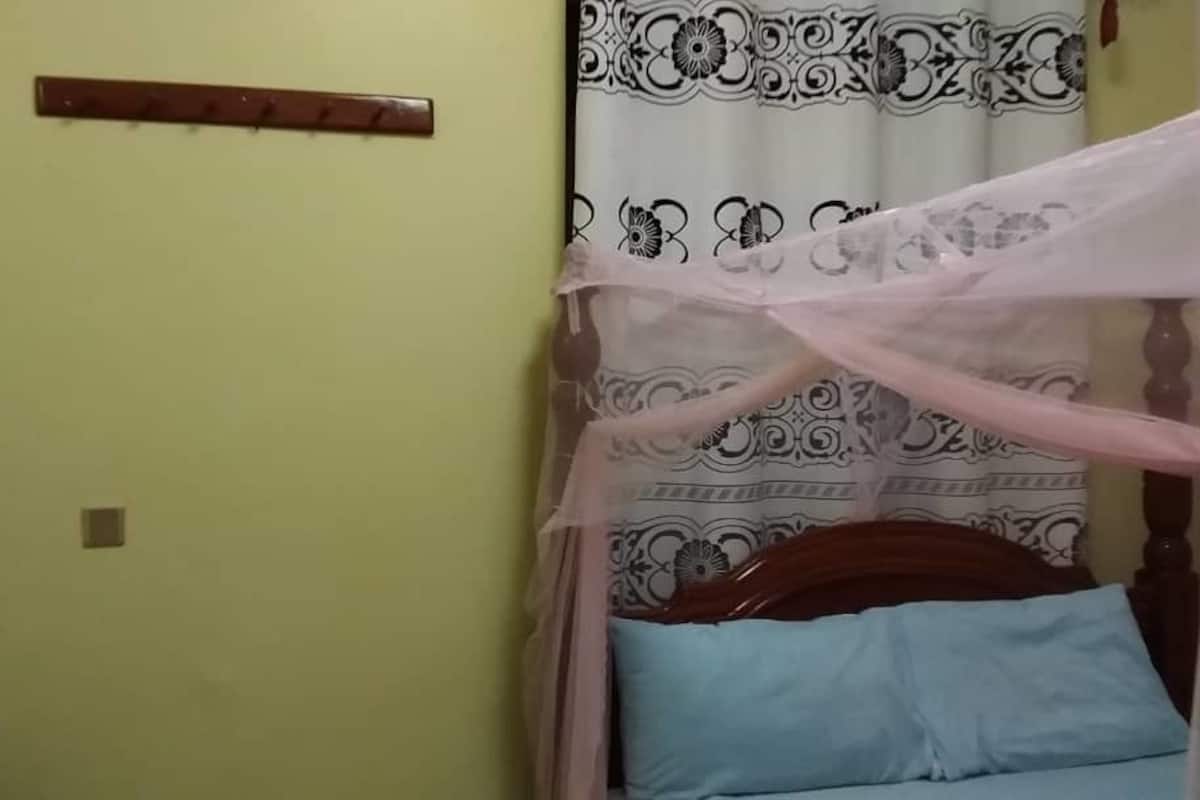 Un dormitorio con una cama, mosquitero y cortina estampada con motivos florales.