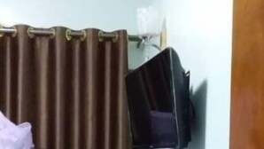A room with a brown curtain, a bed with a white bedspread, and a black object on the wall. - Faida Hill Motel (Kampala)