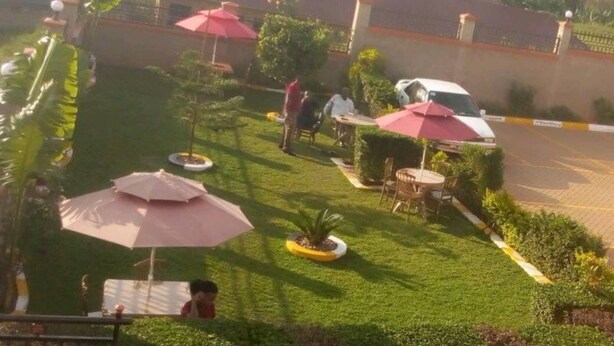A well-maintained garden with neatly trimmed grass, several outdoor umbrellas, and a few people walking around. - Faida Hill Motel (Kampala)