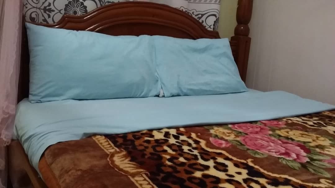 A bed with a light blue mattress and pillows, a brown headboard, and a floral-patterned bedspread.
