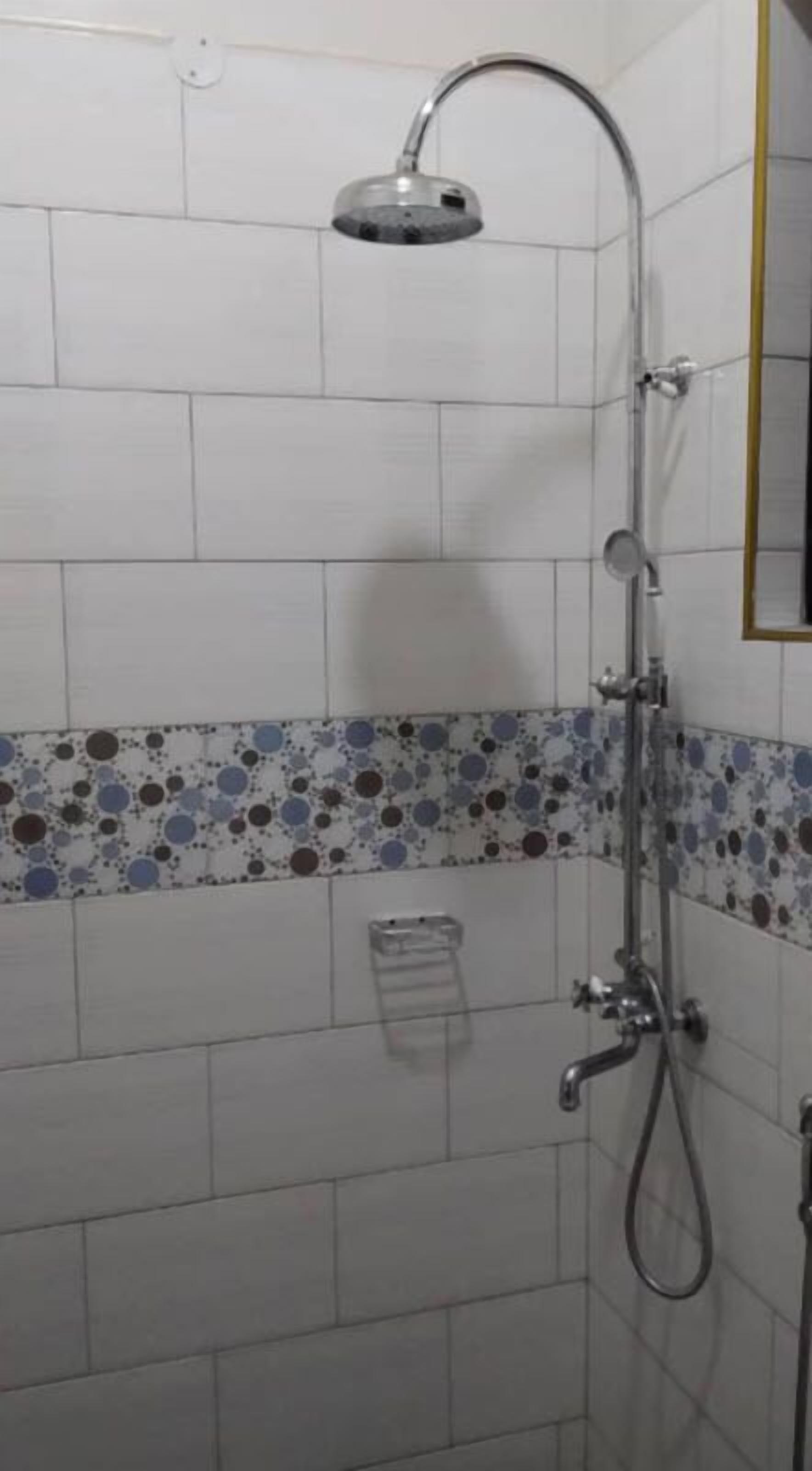 A shower area with a handheld showerhead, a wall-mounted faucet, and a small shelf.
