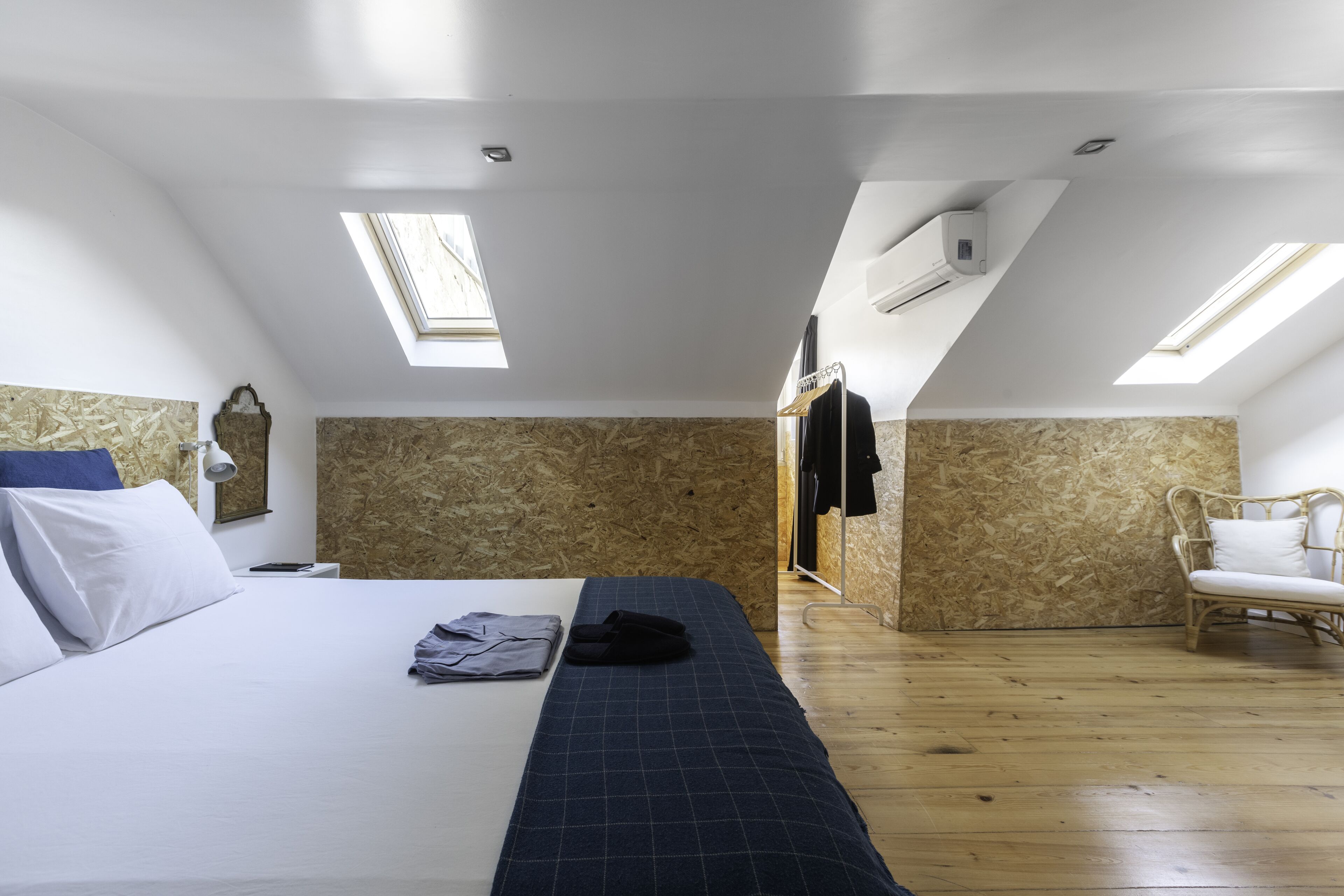 Un dormitorio con una cama, una silla y un armario. Hay tragaluces y una unidad de aire acondicionado en el techo.