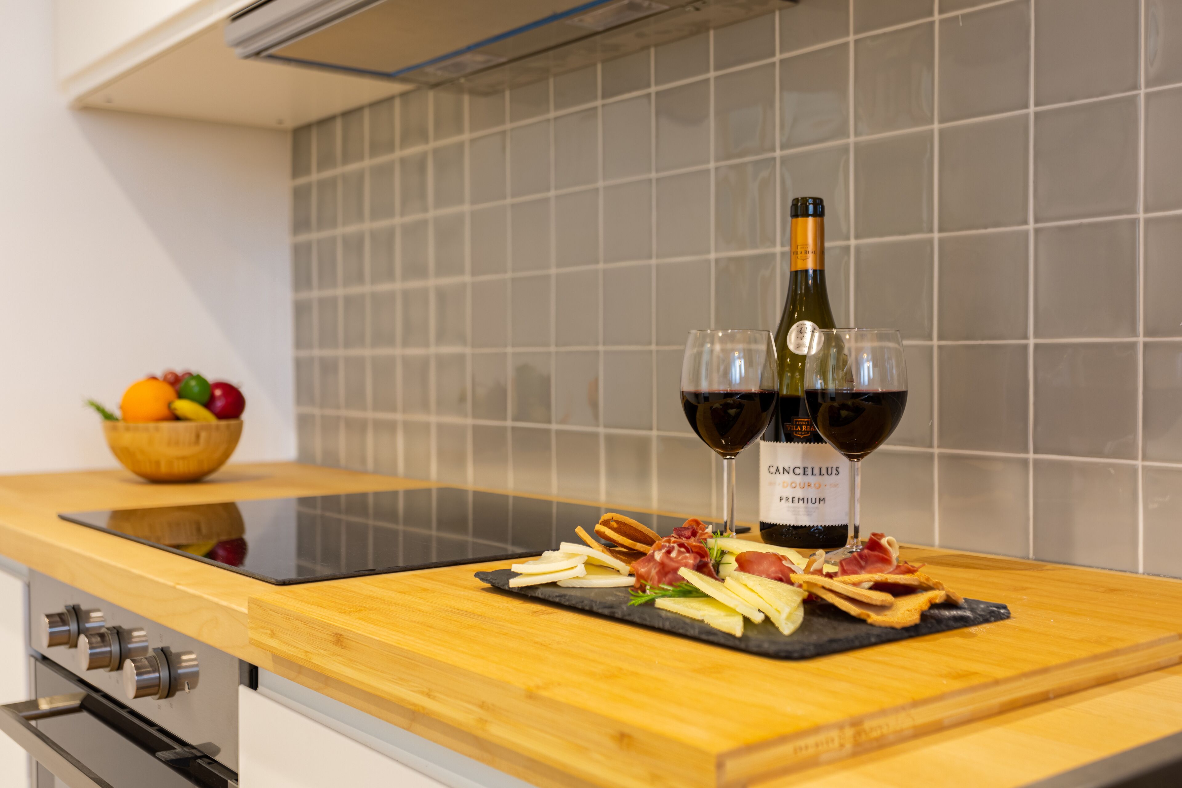 A kitchen counter with a bottle of wine, two glasses, and a fruit bowl.