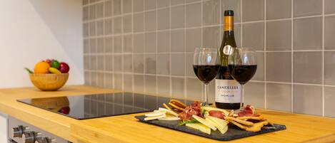 A kitchen counter with a bottle of wine, two glasses, and a fruit bowl.