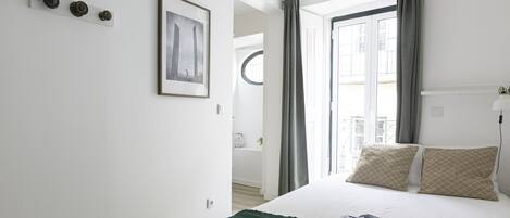 A hotel room with a bed, a framed picture on the wall, and a window with curtains.