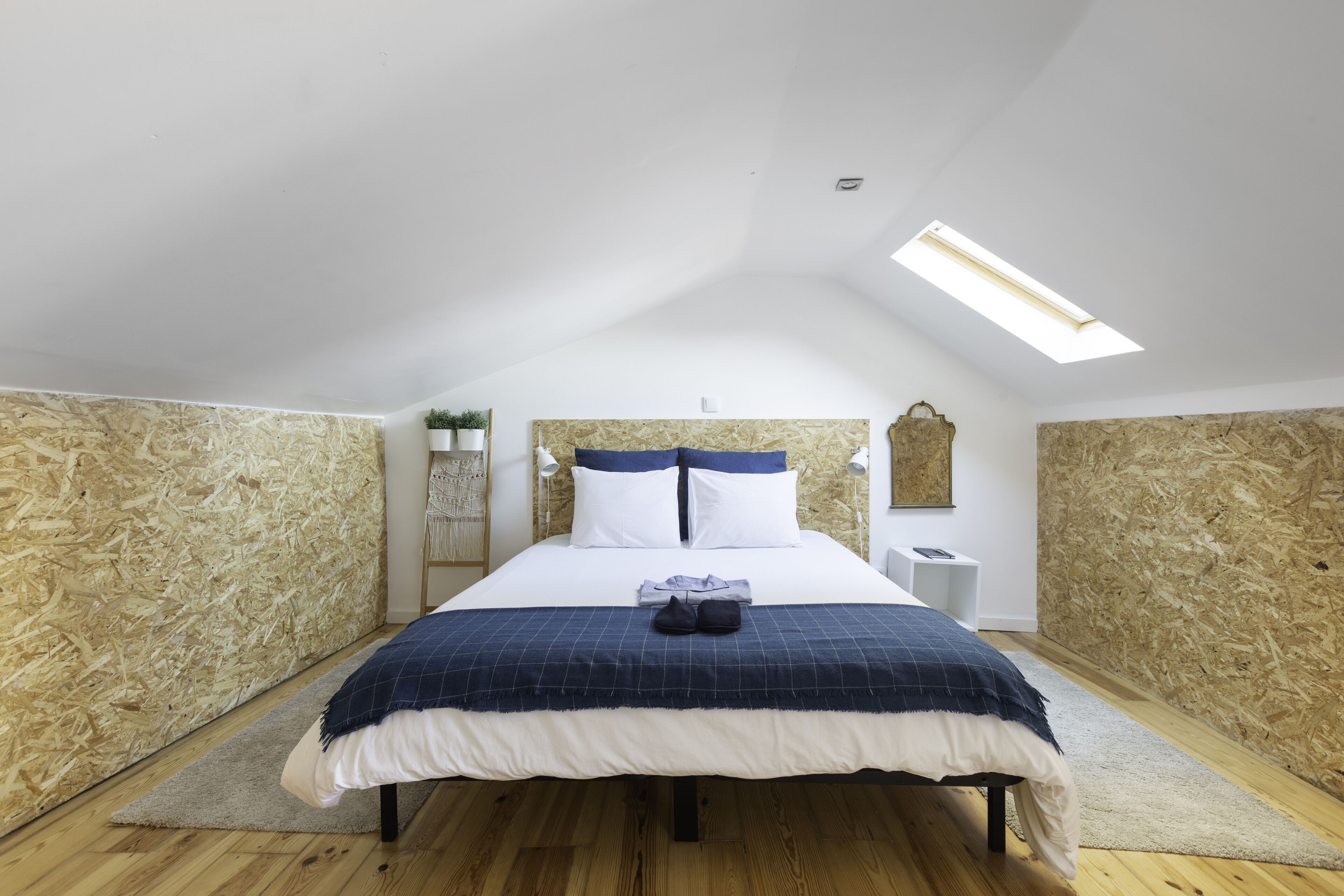 Een slaapkamer met een schuine kap, dakraam, een bed met een blauw-wit geruit dekbed en houten wanden.