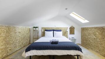 Een slaapkamer met een schuine kap, dakraam, een bed met een blauw-wit geruit dekbed en houten wanden.