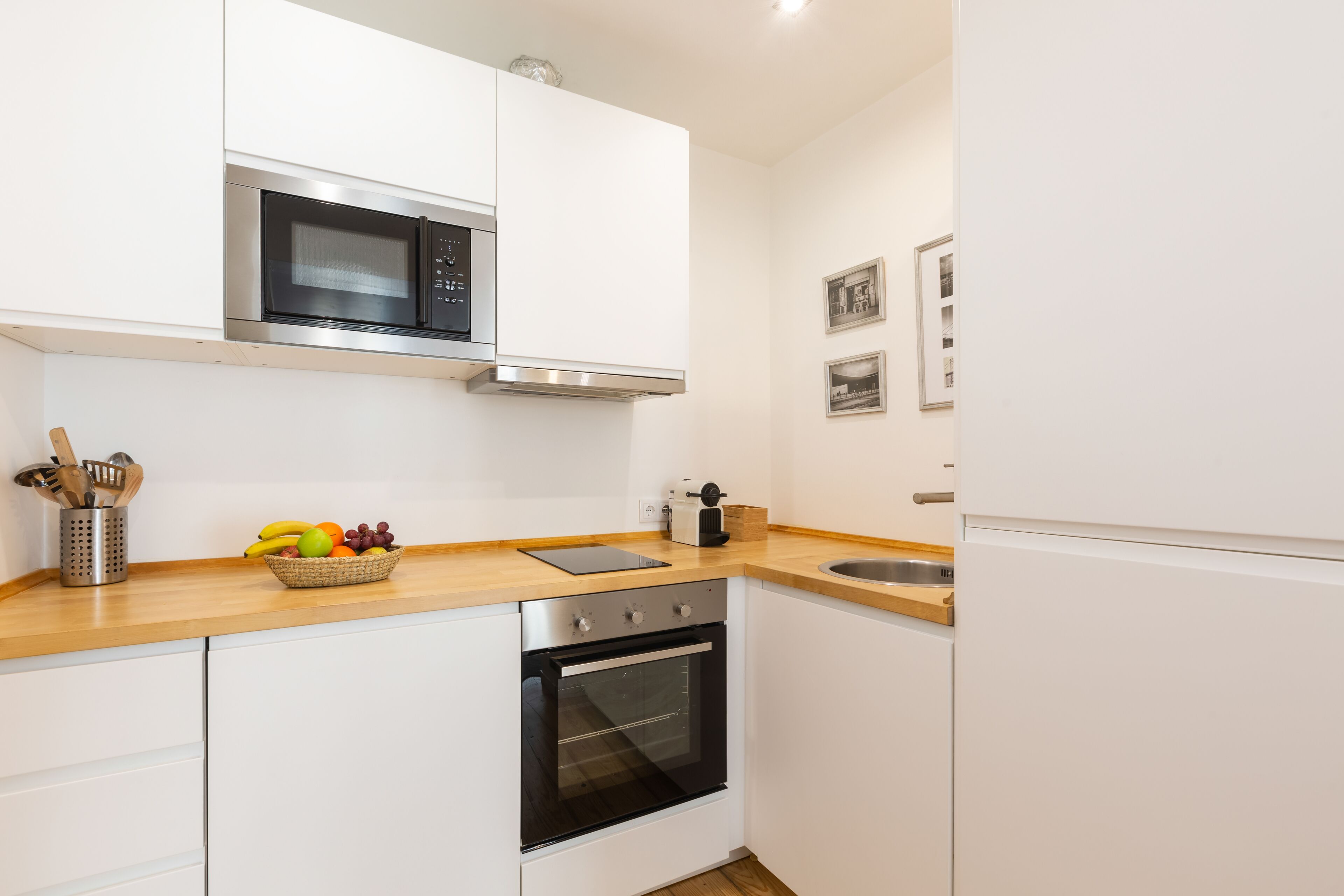 A modern kitchen with white cabinets, a stainless steel oven, a microwave, and a wooden countertop.