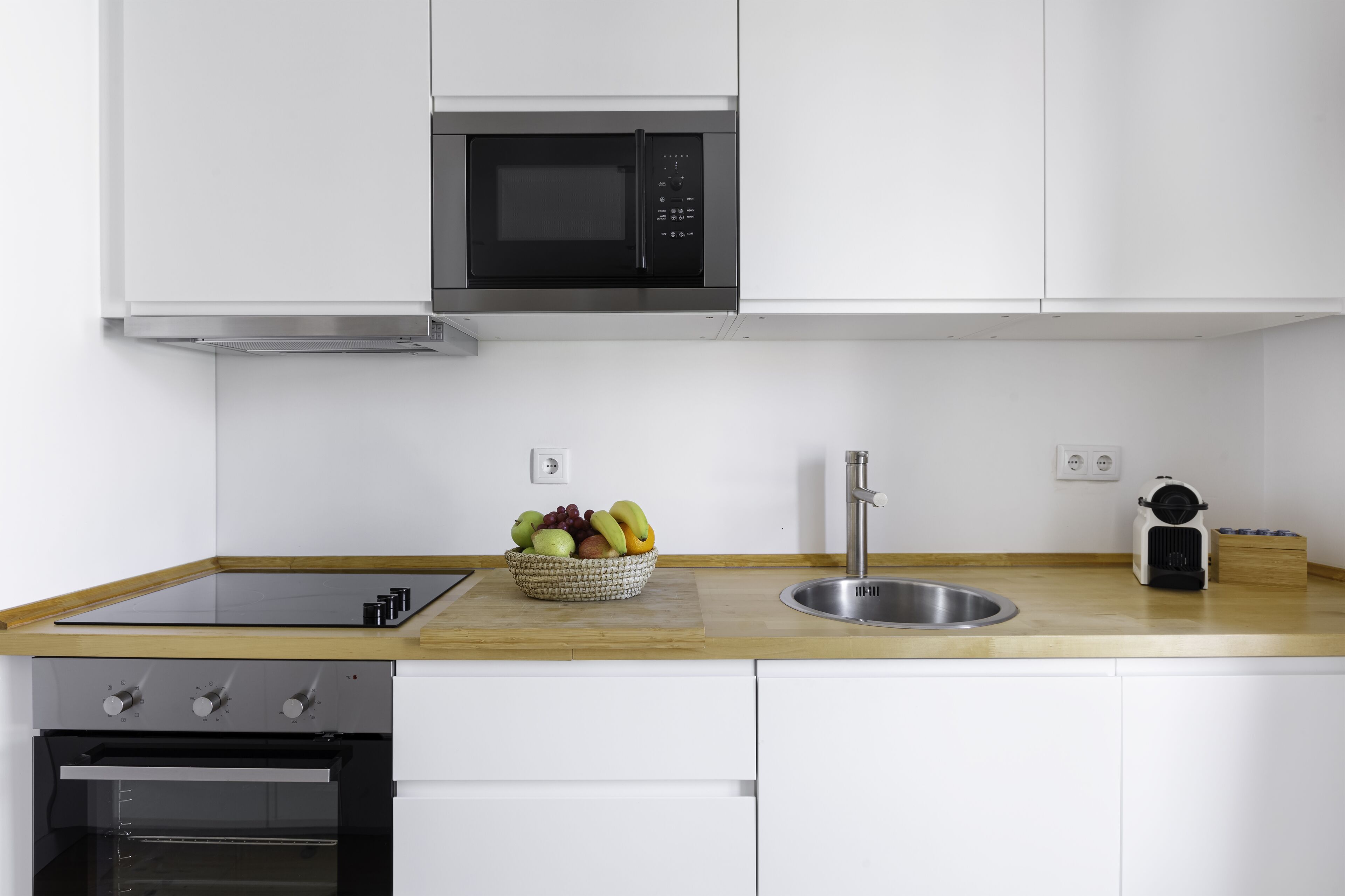 A modern kitchen with a built-in microwave, a sink, and a wooden countertop.